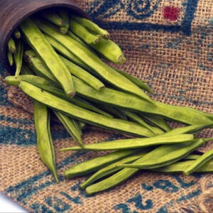 A pot full of green cluster beans kept on a jute rug