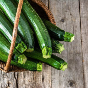 Long green zucchinis kept in a brown basket on a wooden floor