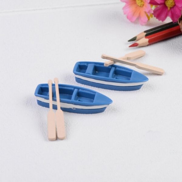 A beautiful and cute two Miniature boats with Oars on a white surface with some colored pencils and flowers beside them.