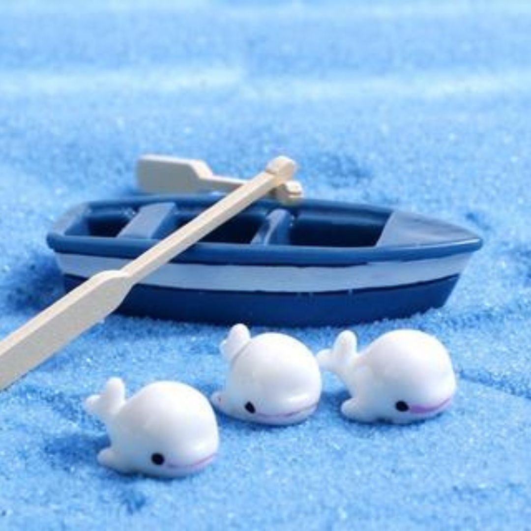 This is an image of cute and small Miniature dolphin on a blue surface with miniature boat with oars in the background.