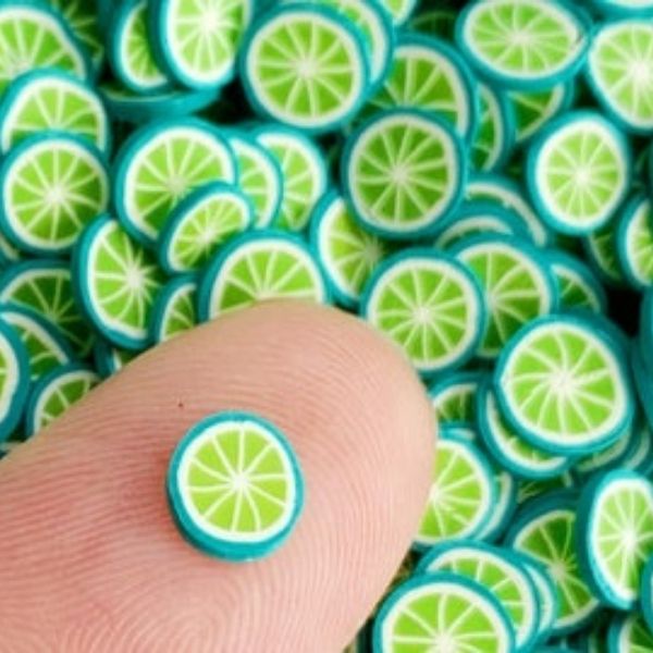 A Miniature Polymer Clay Green Orange on a finger tip with similar several in the background.